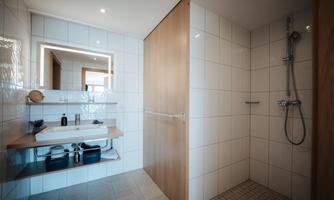 A modern bathroom with a shower and a stylish sink countertop. The walls are tiled with white tiles, and there is pleasant lighting.