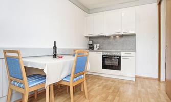 A modern kitchen with bright cabinets and a table with chairs. The floor is made of wood and the walls are painted white.