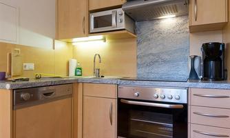 A modern kitchen with wooden cabinets and a bright marble backsplash. It is equipped with a stove, a dishwasher, and a microwave.