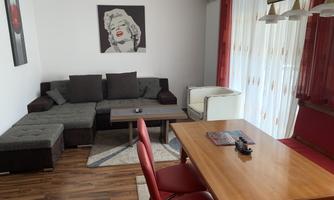 A modern living room with a cozy sofa and a wooden table. A picture of Marilyn Monroe hangs on the wall, and large windows provide plenty of light.