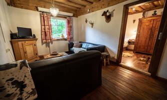 A cozy living room with a wooden ceiling and floor. There is a black sofa, a television, and traditional decorations on the walls.
