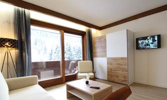 A modern living room with a cozy sofa and a wooden table. Large windows offer a view of snow-covered trees outside.
