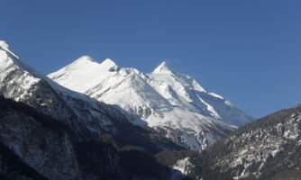 An impressive mountain landscape with snow-covered peaks under a clear blue sky. The surrounding valleys are green and invite exploration.