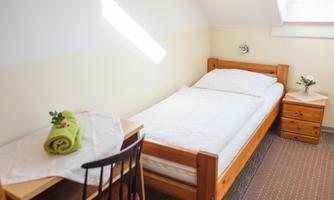 A simple bedroom with a single bed and a small table. The walls are bright, and there is a pleasant table decoration.