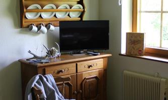A cozy room with a wooden table, a television, and a windowsill. Plates hang on the wall and a chair stands beside it.