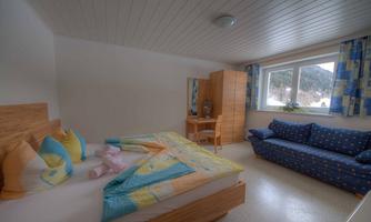 A bright bedroom with a double bed and colorful cushions. In the room, there is a desk and a comfortable sofa.