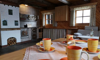 A cozy kitchen with wooden details and a traditional stove. Colorful cups and saucers are on the table, inviting you to enjoy some tea.