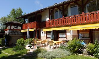 A cozy house with a beautiful garden. There is a terrace with tables, chairs, and umbrellas.