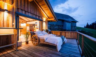 A cozy bedroom on a wooden terrace with a view of nature. The warm light creates an inviting atmosphere at twilight.