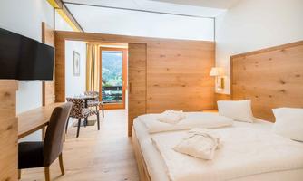 A modern hotel room with wooden paneling and large windows. It is bright and comfortable, featuring a double bed and a workspace.