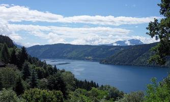 A beautiful lake surrounded by green forests and mountains. The sky is clear and cloudless.