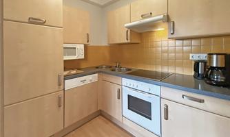 A modern kitchen with light wooden cabinets and an orange tiled backsplash. The equipment includes a stove, an oven, and a microwave.