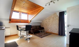 A cozy attic room with a wooden ceiling and large windows. There is a modern dining area and a sofa for relaxation.