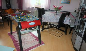 A cozy living space with a table football game and a dining table. In the background, comfortable furniture and floral arrangements can be seen.