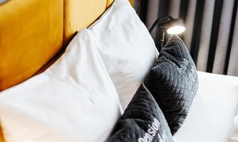 A cozy bed with bright cushions and decorative gray pillows. The wall is elegantly designed with a floral pattern.