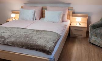 A cozy bedroom with a double bed and two bedside tables. Next to the bed is an armchair and there is soft lighting.