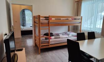 A cozy room with a bunk bed and a dining table. There is a television and large windows that let in a lot of light.