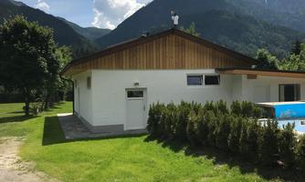 A modern house in a green landscape with mountains in the background. The sky is clear and partially cloudy.