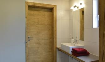 A modern bathroom with wood and tile elements. There is a sink, a mirror, and a wooden door.