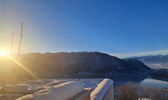 A beautiful winter morning with snow-covered mountains. The sun rises over the calm lake and bathes the landscape in warm light.
