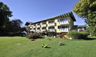 A modern building with several balconies in a green garden landscape. The surroundings are sunny and inviting, ideal for relaxing stays.