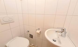 A small bathroom with a toilet and a sink. The walls are tiled white, and the floor has a pattern of small stones.