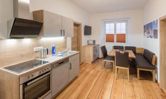 A modern kitchen with wooden fronts and a dining area. Large windows provide plenty of light in the room.