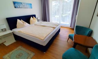 A cozy bedroom with a double bed and two pillows. There is a beautiful view of the outdoor area through large windows.