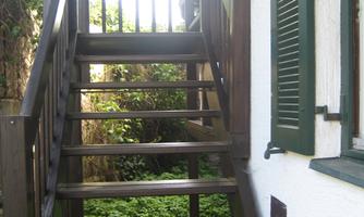 A wooden staircase leads to an upper floor. In the background, green plants can be seen.
