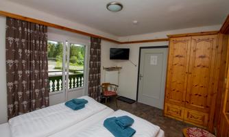A cozy room with two single beds and blue towels. Large windows offer a view outside, and there is a television on the wall.