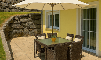 A cozy outdoor area with a table and chairs under a sun umbrella. The wall of the apartment is painted in a warm shade of yellow.