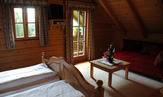 A cozy room with two single beds and a red couch. Large windows let in plenty of light and the walls are made of wood.