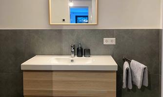 A modern bathroom with a wooden vanity and a large mirror. Towels hang on the wall next to the sink.