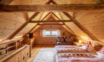 A cozy attic room with wooden paneling and a vaulted ceiling. Two beds with checkered bedspreads and a warm, inviting atmosphere.