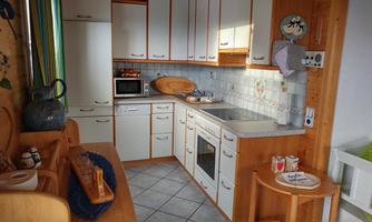 A bright, modern kitchen with white cabinets and a gray tile backsplash. There is a microwave, an oven, and some kitchen utensils on the countertop.