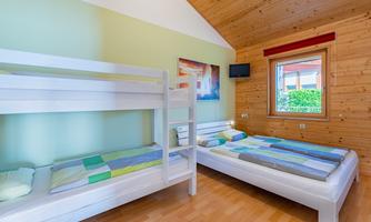 A bright bedroom with a bunk bed and a single bed. The walls are painted in soft colors, and a window lets in plenty of light.
