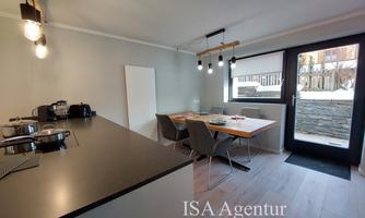 Modern kitchen with a counter and a dining area. Bright, open atmosphere with large windows and a view outside.