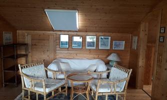 A cozy room with wooden walls and a light floor. There is a sofa, two chairs, and some pictures on the wall.