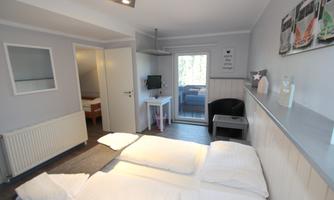 A bright room with two beds and a balcony. The walls are designed in soft colors and there is modern furniture.