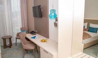 A modern hotel room with a cozy desk and a television. Fresh fruit is placed on the table, and the decor is bright and inviting.