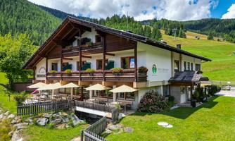A beautiful building in the Alps with balconies and terraces. The surroundings are filled with green meadows and trees, perfect for a peaceful stay.