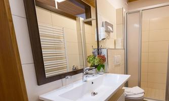 A modern bathroom with a white sink and a shower. The walls are brightly tiled, and a mirror reflects the space.