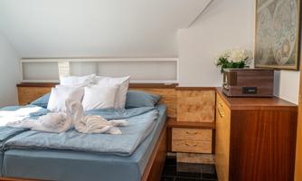 A cozy bedroom with a large bed and soft pillows. Next to the bed stands a wooden dresser and a floral arrangement on the table.