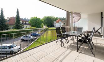 A modern terrace with a large table and chairs. In the background, trees and houses can be seen.