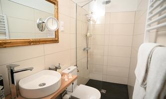 A modern bathroom with a shower, sink, and a large mirror. The walls are brightly tiled and there is a towel rack.
