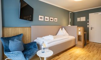 A modern room with a large window and a cozy armchair. A flat-screen TV is mounted on the wall and fresh towels are placed on the bed.