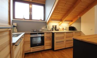 The kitchen has wooden cabinets and a bright, friendly atmosphere. Large windows provide plenty of natural light.