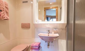 A modern bathroom with a sink, a toilet, and a mirror. Soft, pink towels are neatly stacked.