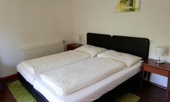 A cozy bedroom with a double bed and two nightstands. The walls are light, and a carpet is on the floor.