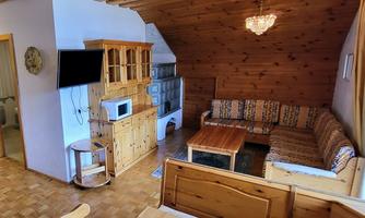 A cozy living room with wood paneling and a sofa. In the room, there is a dining table, a microwave, and a television.